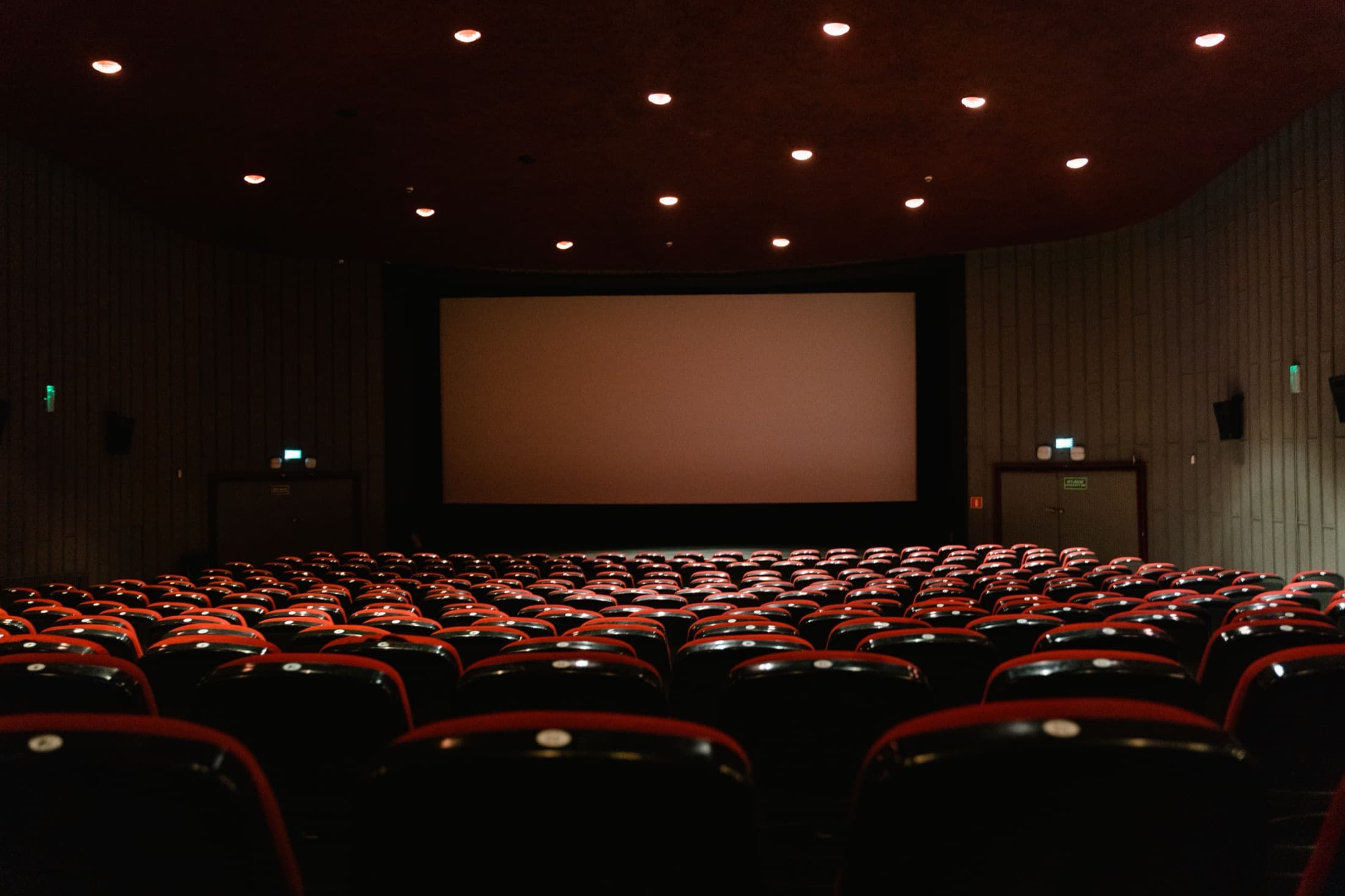 An empty cinema, curved rows of seats facing a lit screen.