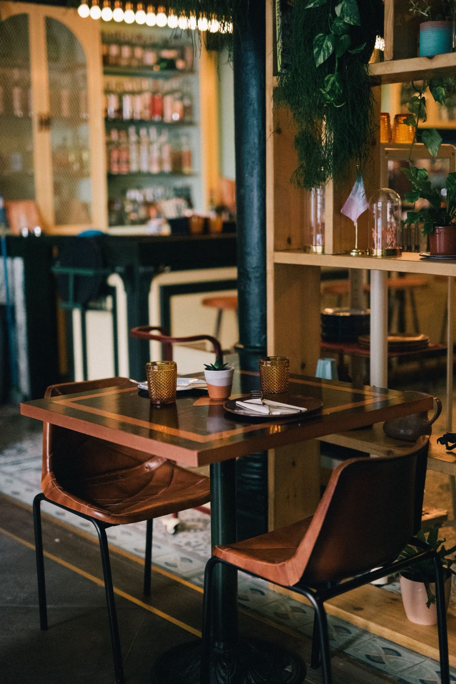 A table laid for two in an empty restaurant, bar shelves behind.