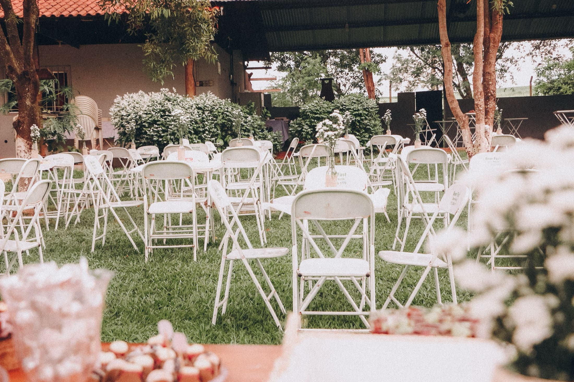 Rows of white folding chairs set out on grass for an outdoor event, nobody seated.