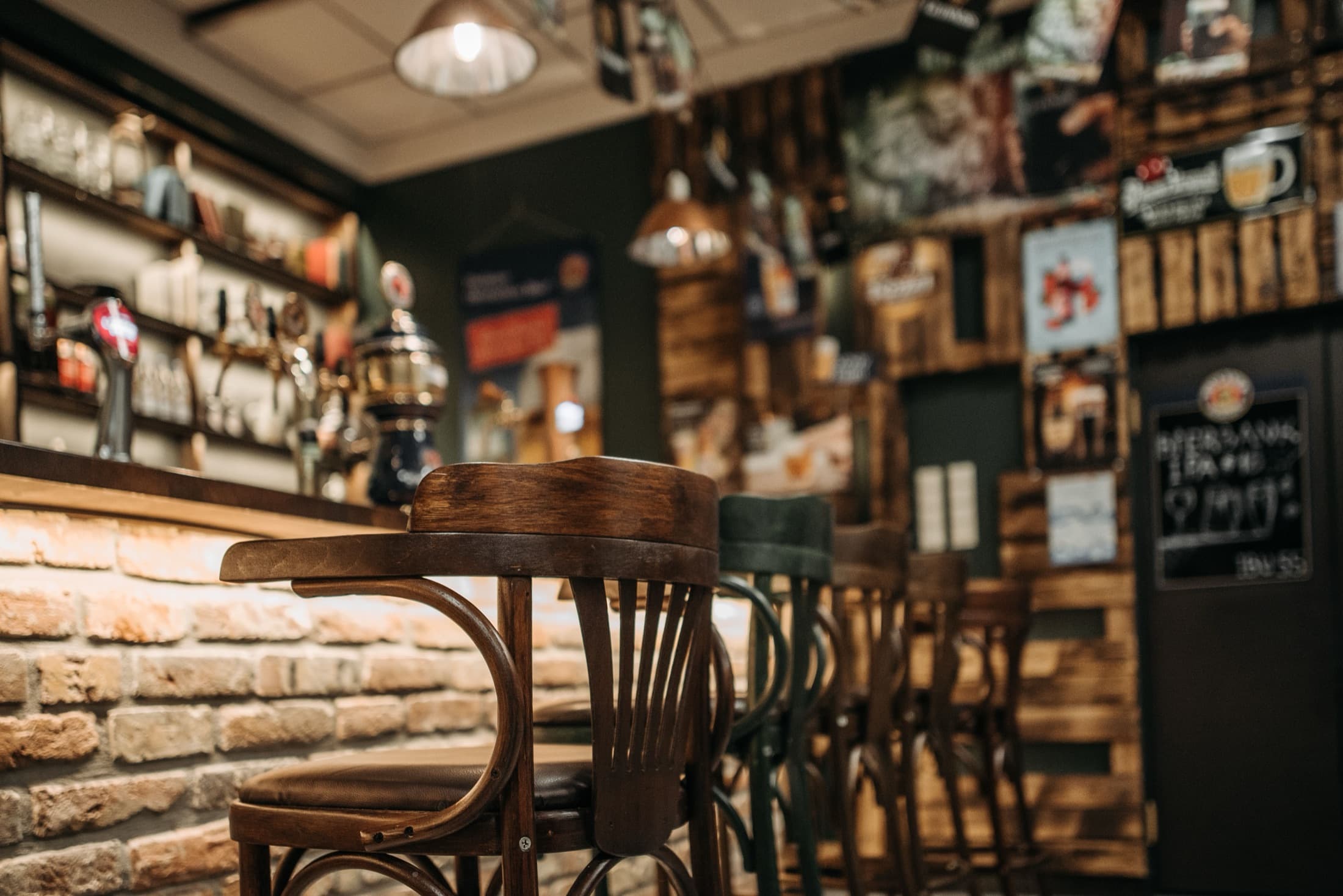 The bar of an empty pub, stools pushed in along a brick counter.